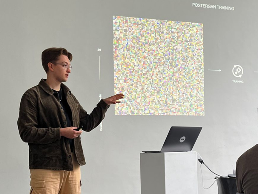 Samuel is standing next to a laptop and pointing at images that are projected on the wall.